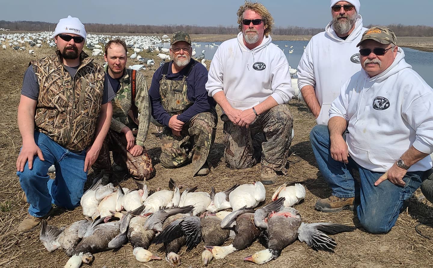 six male hunters kneeling next to an assortment of geese